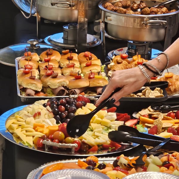 A hand serving from a buffet of sliders, fruit, cheese, and meatballs at Pipilinka.