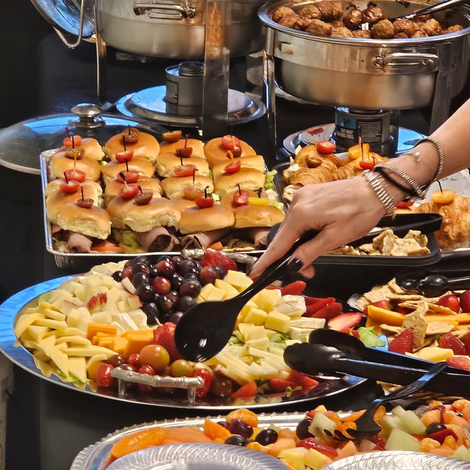 A hand serving from a buffet of sliders, fruit, cheese, and meatballs at Pipilinka.