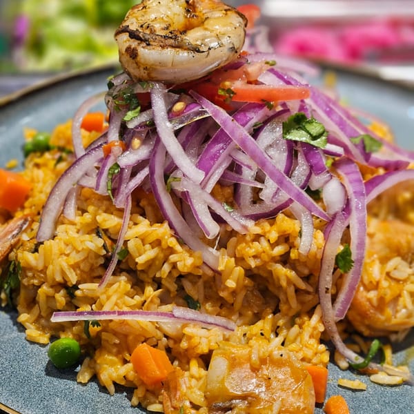 Peruvian arroz con mariscos with grilled shrimp, red onions, tomatoes, and cilantro on a blue plate.