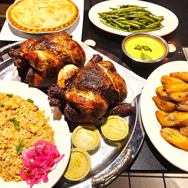Peruvian roasted chicken, fried rice, plantains, green beans, and a golden pie on a dark table.