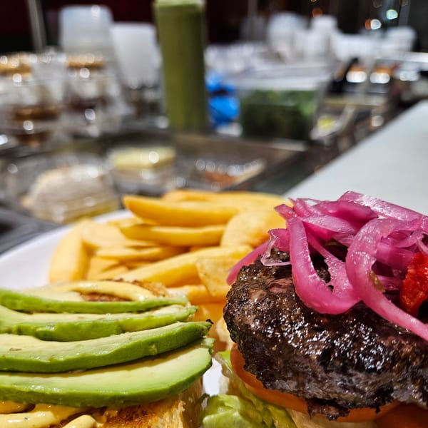 A Peruvian burger with avocado, pickled red onions, and a side of fries.