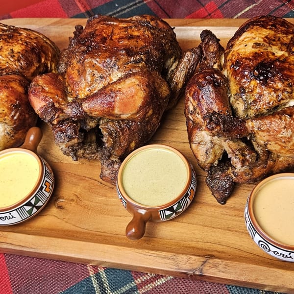 Three whole Peruvian rotisserie chickens with crispy skin and three dipping sauces on a wooden tray.